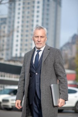 Gri saçlı, gri ceketli adam iyi görünüyor.