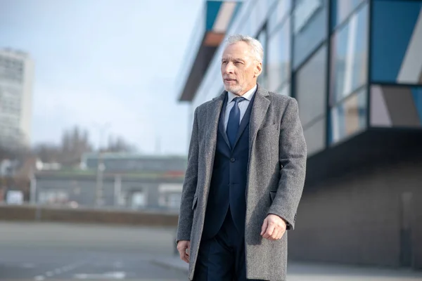 Hombre de pelo gris con un abrigo gris de pie cerca de la oficina — Foto de Stock