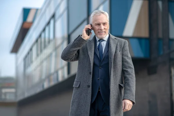 Hombre de pelo gris con un abrigo gris hablando por teléfono — Foto de Stock