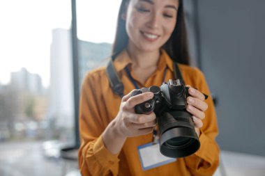 Koyu saçlı, genç, sevimli muhabir kameradaki fotoğraflara bakıyor.