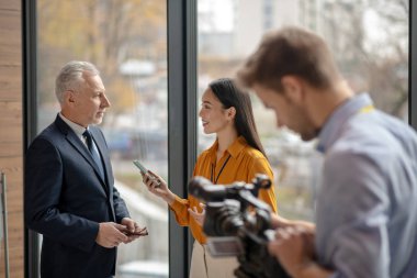 Asyalı kadın muhabir mikrofon tutuyor ve gülümsüyor.