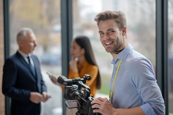 Masculino jovem operador com câmera de vídeo olhando satisfeito — Fotografia de Stock