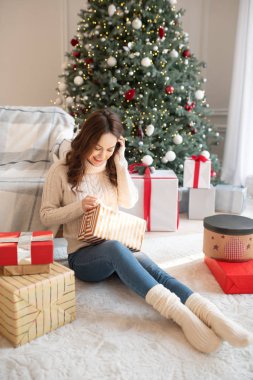 Koyu saçlı genç kadın Noel hediyelerini açıyor.
