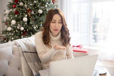 Koyu renk saçlı, açık renk kazaklı güzel bir kadın bir video görüşmesi yapıyor.