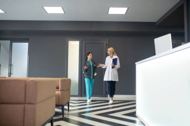 Kıdemli doktor ve genç stajyer koridorda bilgi paylaşıyorlar.