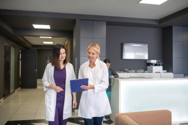 Klinik koridorunda konuşan iki kadın doktor.