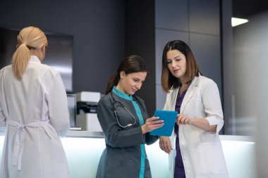 Genç, siyah saçlı kadın doktor elinde bir tablet tutuyor.