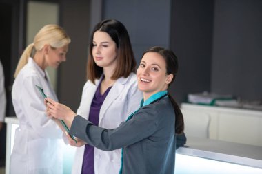 Üç kadın doktor nöroloji kliniğinde resepsiyonda konuşuyor.