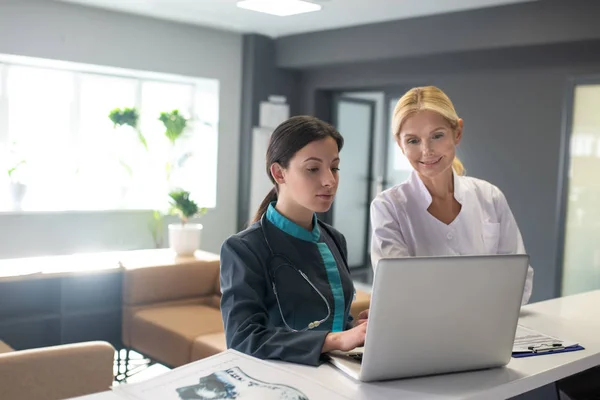 Jonge vrouwelijke stagiaire en blonde arts op zoek naar informatie op internet — Stockfoto