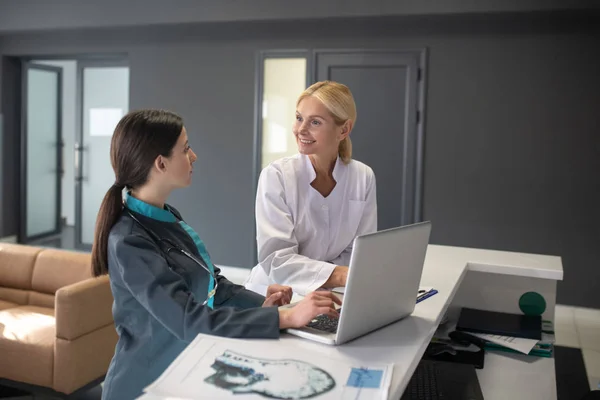 Ung kvinnlig praktikant och blond läkare sitter vid bordet — Stockfoto