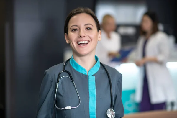 Mladý roztomilý tmavovlasý lékař vypadá šťastně a usmívá — Stock fotografie