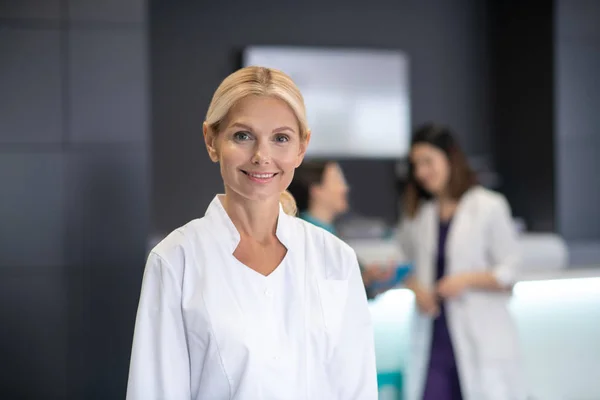 Зріла блондинка лікар в білому халаті посміхається — стокове фото