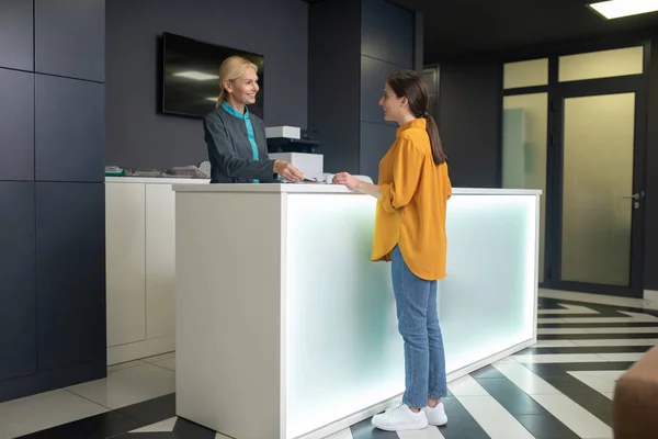 Blond receptionist in clinic greeting a new comer — Stock Photo, Image