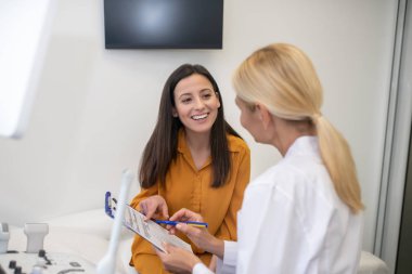 Beyaz cüppeli sarışın doktor ultrason sonuçlarını hastaya söylüyor.