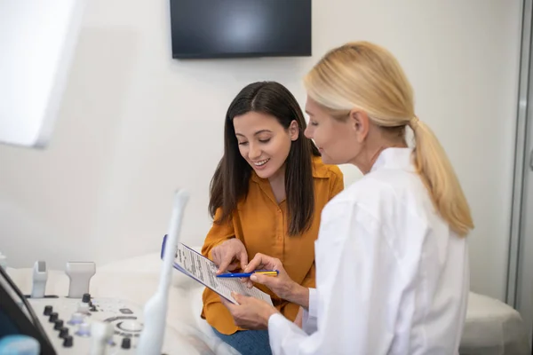 Блондинка лікар в білому халаті показує результати ультразвуку пацієнту — стокове фото