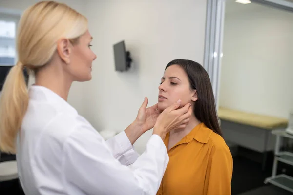 Blond female doctor palping lymth nodes of the patient