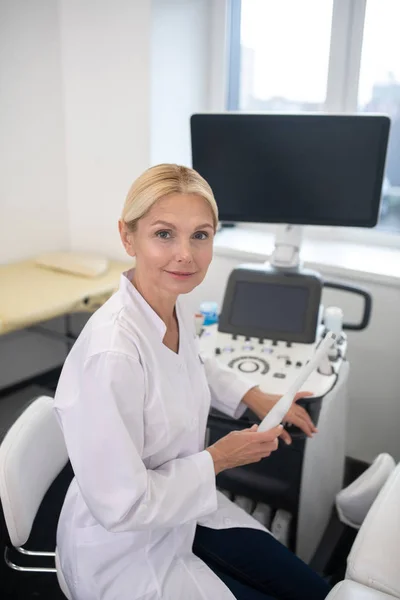 Especialista em ultrassom em roupão branco sentado perto da máquina de ultra-som — Fotografia de Stock