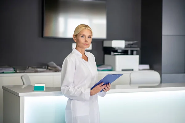 Блондинка красивий лікар в білому халаті, що стоїть біля рецепції — стокове фото