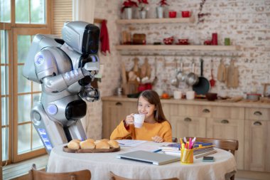 Gülümseyen kız ve robot birlikte çay içiyorlar.