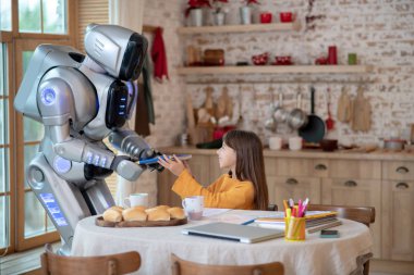 Ev robotu gülümseyen bir kıza kitap veriyor.