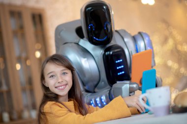 Tabletli robot ve mutfakta oturan gülümseyen bir kız.