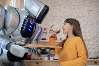 Ev robotu tarafından pişirilmiş köfte deneyen turuncu tişörtlü tatlı kız.