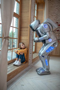 Robot turuncu gömlekli bir kızla konuşuyor.