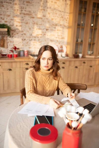 Dark-haired serious young woman in sweater sitting in the kitchen — Stock Photo, Image