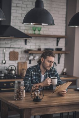 Genç yakışıklı adam mutfağında eski mektupları okuyor.