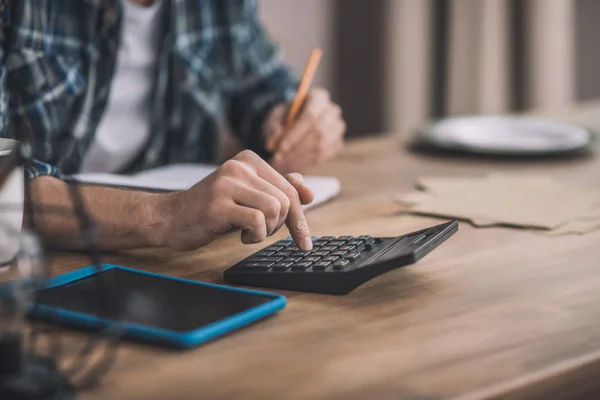 Homem usando um calc e outros gadgets para estimativa financeira — Fotografia de Stock