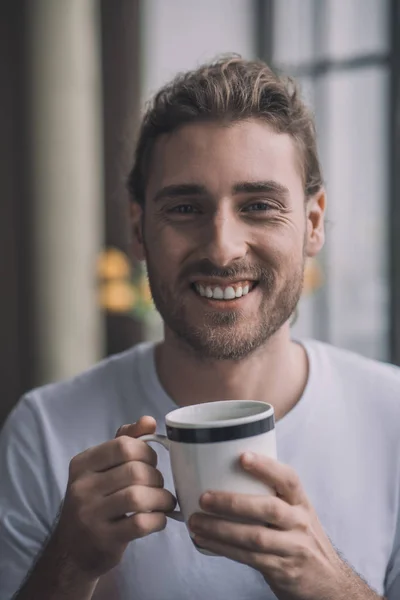 Pensativo hombre sonriente bebiendo su taza de café de la mañana . — Foto de Stock