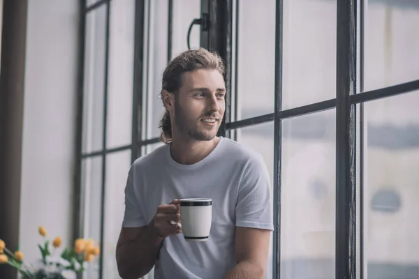 Inspirerad långhårig man som tar en kopp morgonkaffe. — Stockfoto