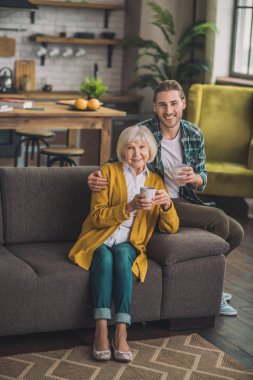 Beyaz saçlı yaşlı kadın oğluyla kanepede oturuyor.