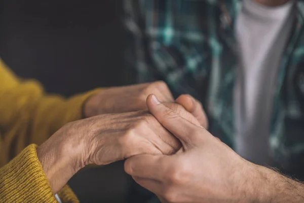 Young man tenderly holding his moms hands — Stock Photo, Image