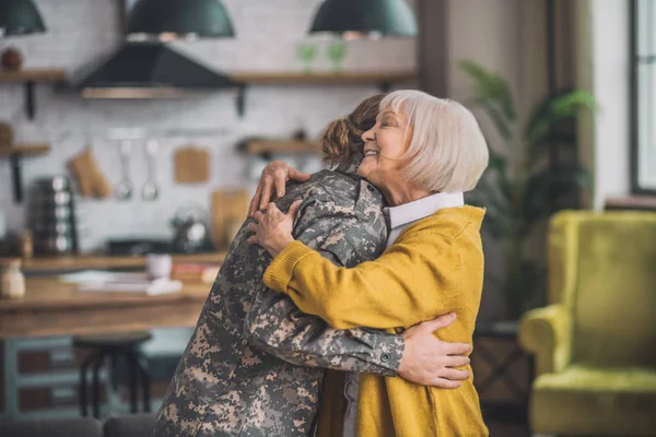 Mom in yellow shirt hugging her son in uniform — Stock Photo, Image