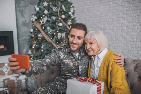 Sonriente hombre en uniforme de camuflaje haciendo selfie con mamá — Foto de Stock