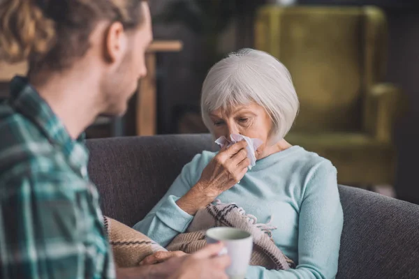 Grey-haired elderly woman cleaning her nose with napkin — Stock Photo, Image