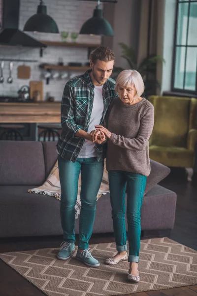 Young man in jeans helping his mom to walk — Stock Photo, Image