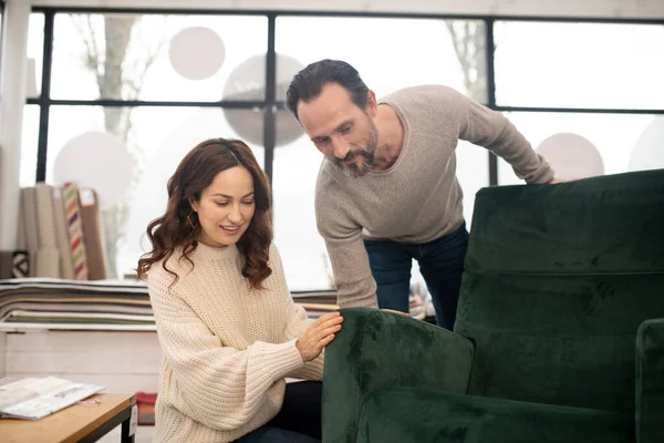 Homem e mulher em blusas leves examinando uma grande poltrona verde — Fotografia de Stock