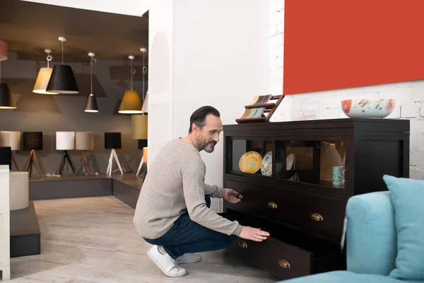 Dark-haired positive man in white snickers opening the drawers — Stock Photo, Image