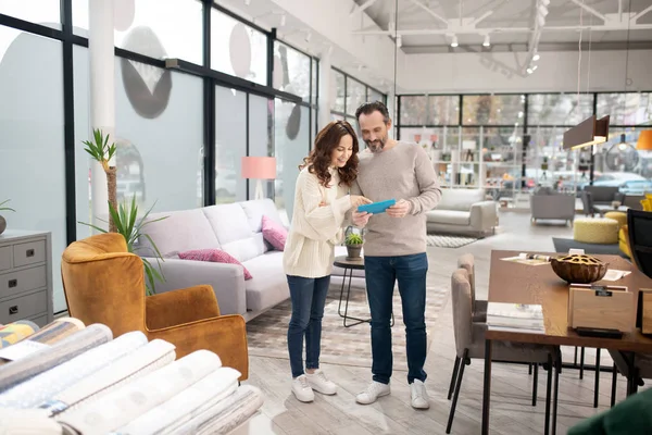 Pareja de pie en el salón de muebles viendo algo en internet —  Fotos de Stock