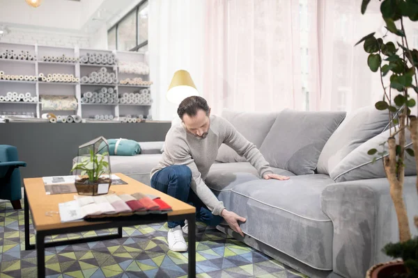 Man in light sweater and jeans examining the sofa — 스톡 사진