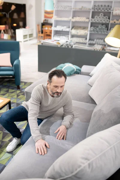 Man in light sweater and jeans touching the sofa — 스톡 사진