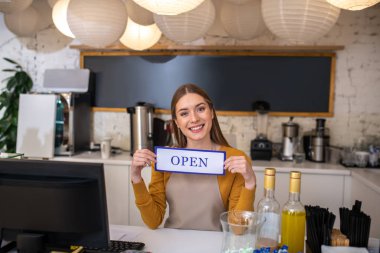 Gülümseyen genç barista açık tabelayı tutuyor.
