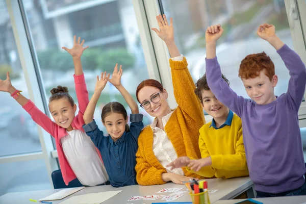 A tanár és a gyerekek felemelik a kezüket az osztályban. — Stock Fotó
