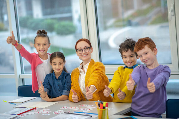 Happy schoolchildren and teacher showing thumbs up