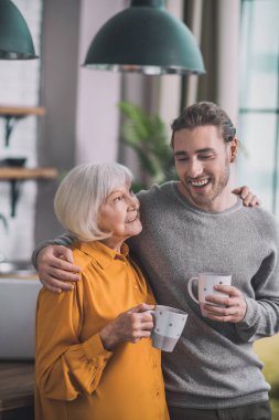 Gri gömlekli genç yakışıklı bir adam ve annesi birlikte harika hissediyorlar.