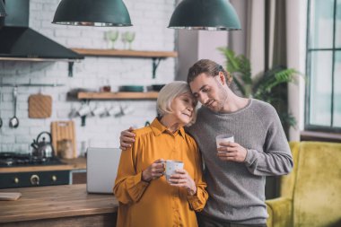 Gri gömlekli genç yakışıklı adam ve annesi birlikte harika hissediyorlar.