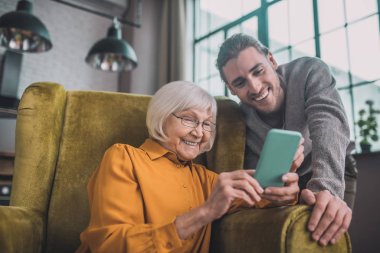 Sarı elbiseli yaşlı bayan akıllı telefon kullanmayı öğreniyor.