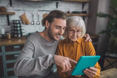 Gri tişörtlü genç yakışıklı adam ve annesi interneti araştırıyor.